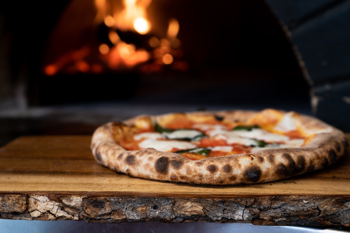 Neapolitanische Pizza auf einem Holzbrett vor dem lodernden Feuer des Holzofens