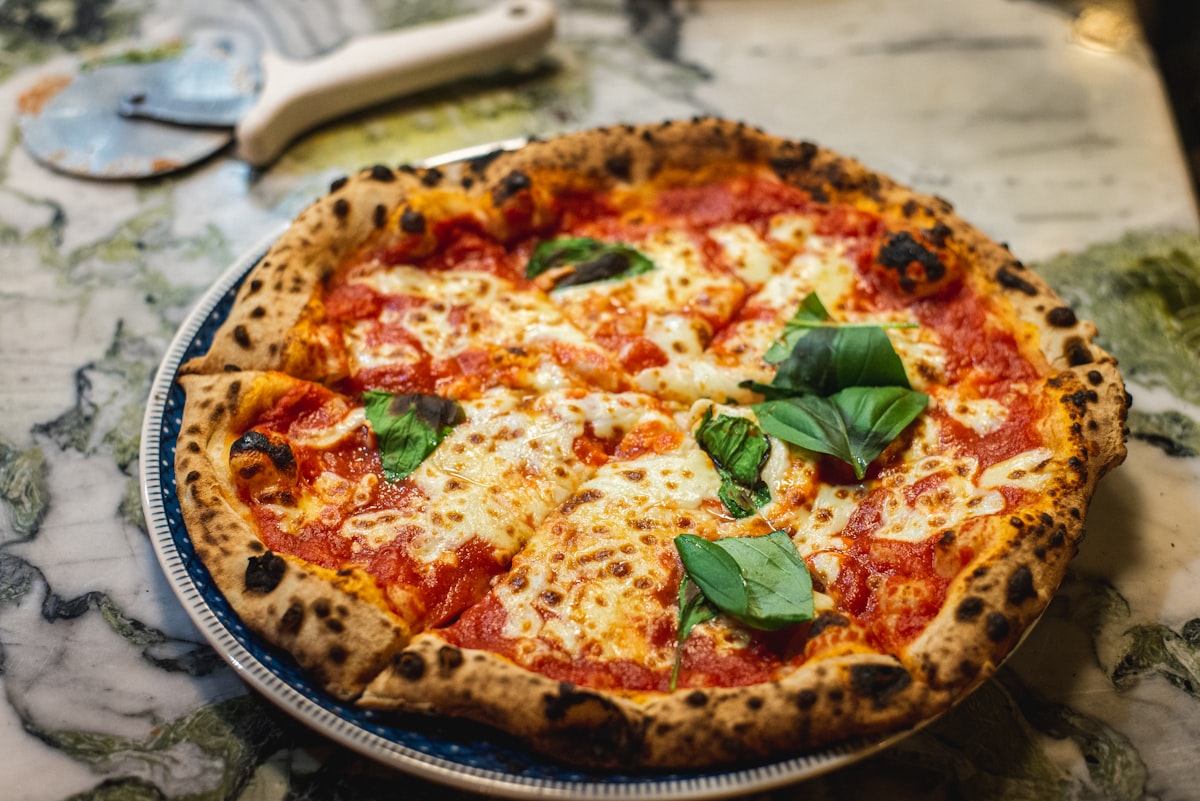 Pizza mit leopardgeflecktem Rand und Basilikum auf hellem Marmortisch