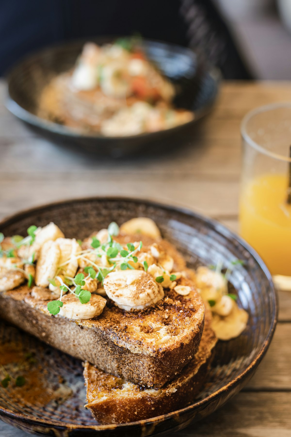 Warmes Bananenbrot French Toast mit karamellisierten Bananen und Microgreens in dunkler Schale