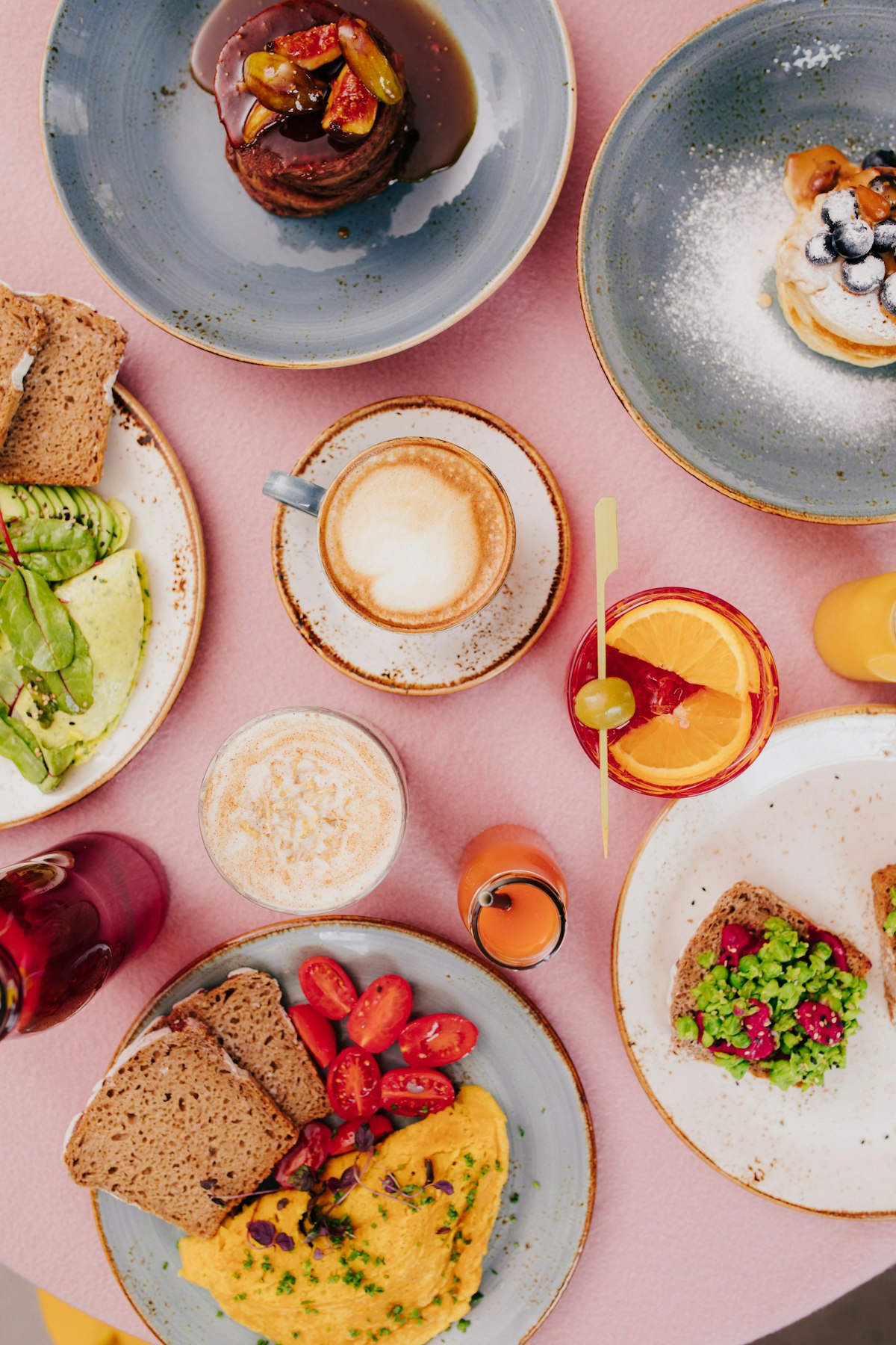 Avocado-Toast und Erbsen-Toast auf rosa Tisch, dazu Smoothie und frischer Orangensaft