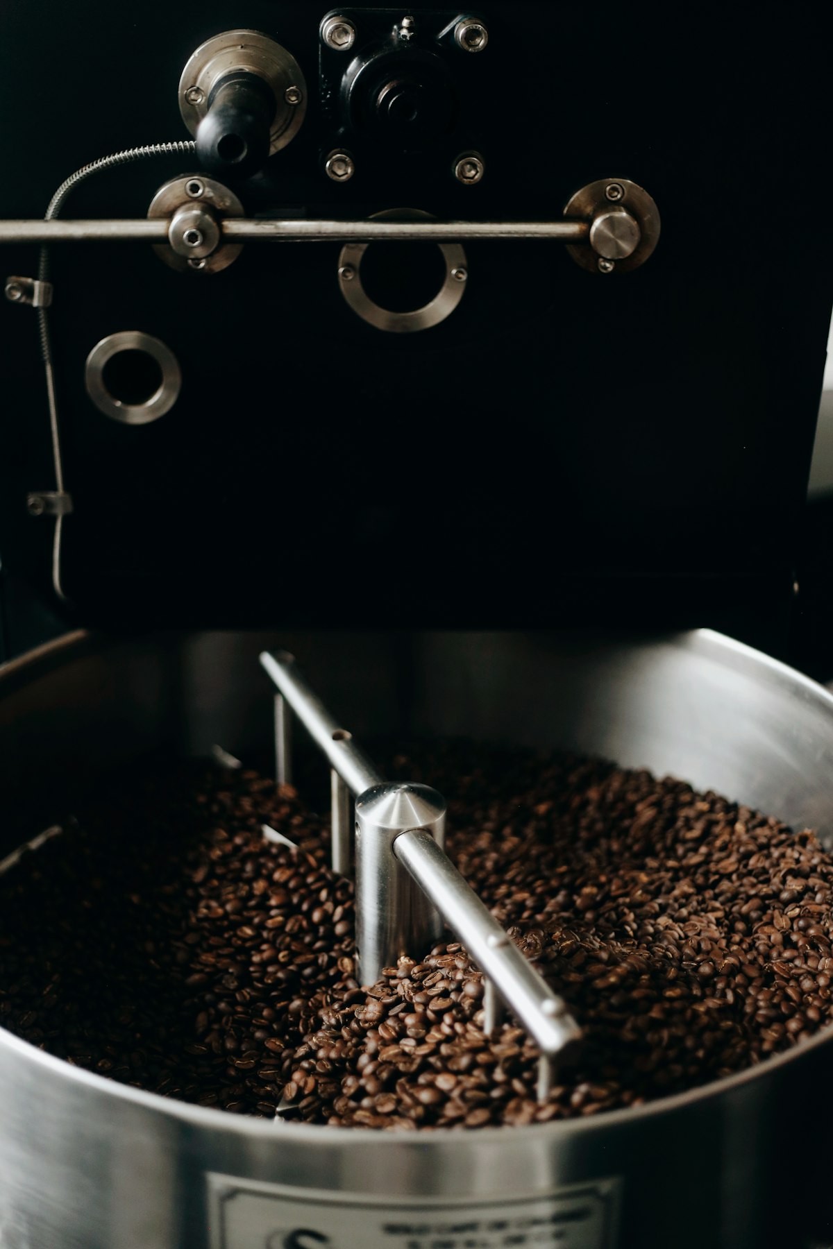 Frisch gerösteter Kaffee im Kühlsieb der Trommelröstmaschine, warme Brauntöne im Halbdunkel der Rösterei