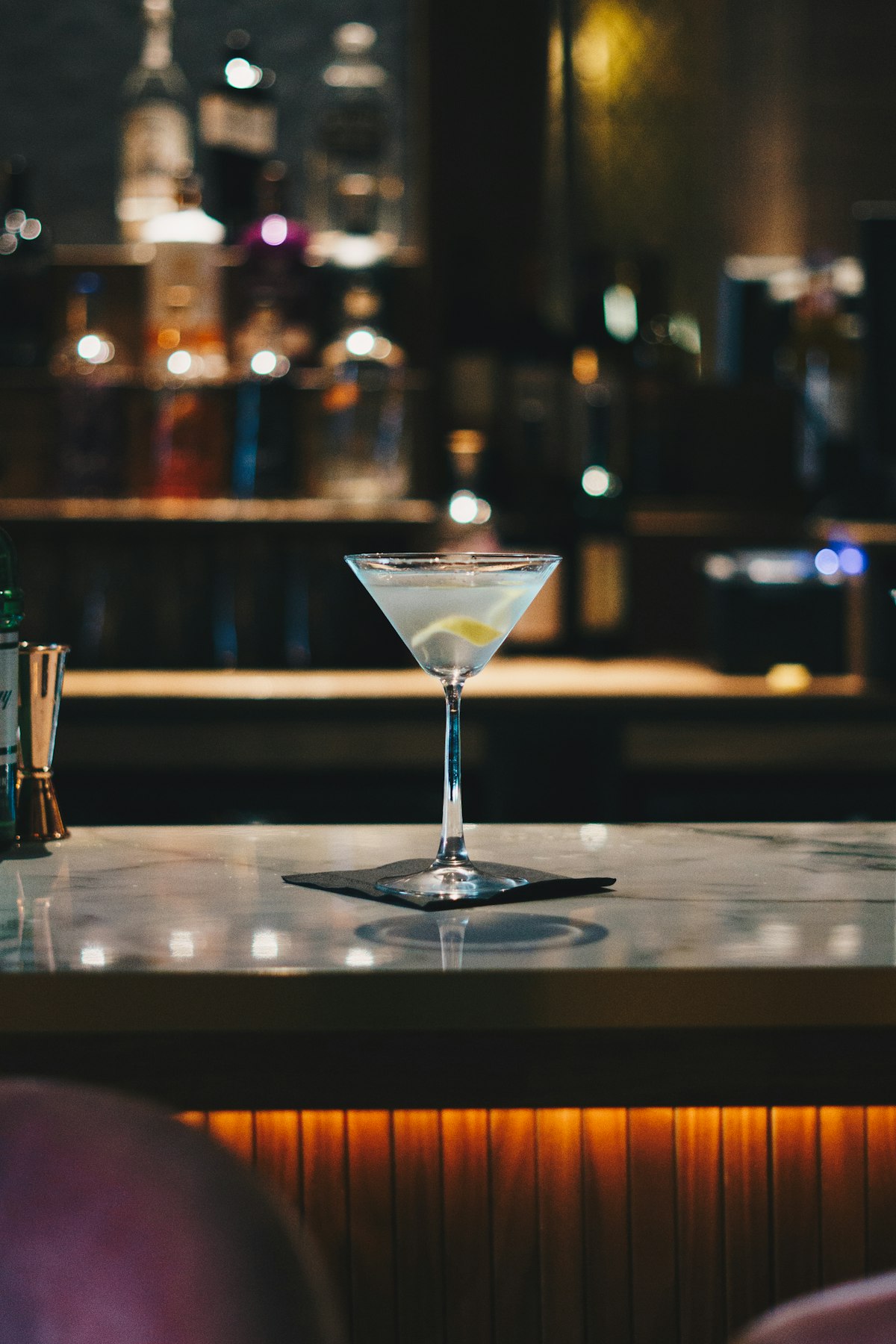 Ein Martini im Kerzenlicht auf einer Marmortheke vor einem unscharfen, dunklen Flaschenregal