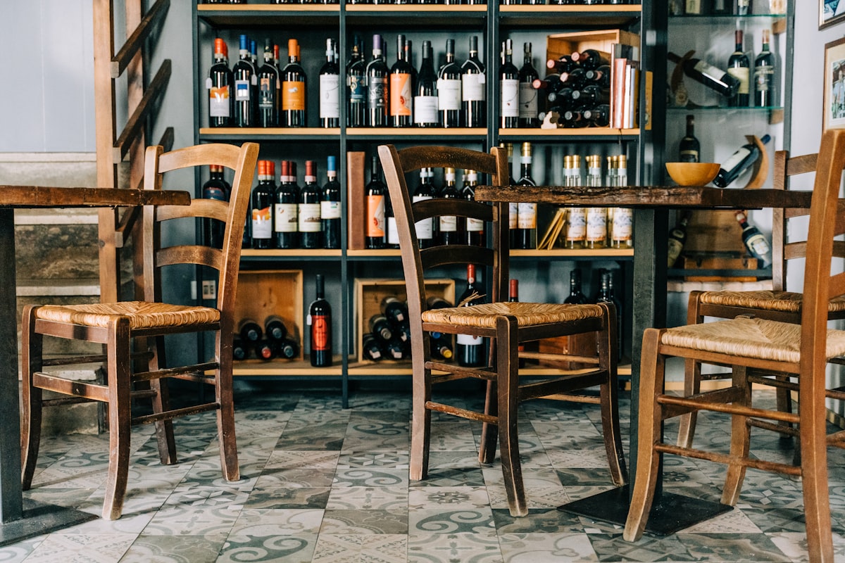 Weinregal mit offenen Flaschen, rustikale Holzstühle mit Binsengeflecht und gemusterte Bodenfliesen im Bistro