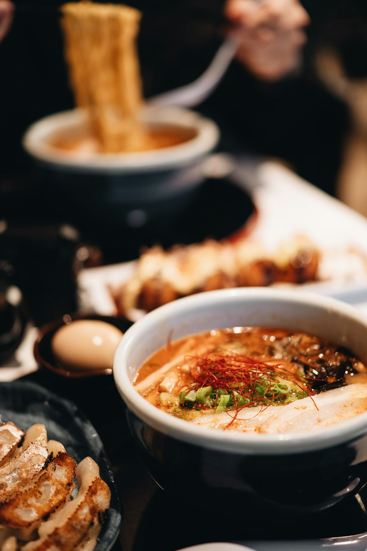 Dunkle Izakaya-Szene bei Nacht, eine scharfe Ramen-Brühe mit roten Chilifäden und Gyoza im warmen Licht