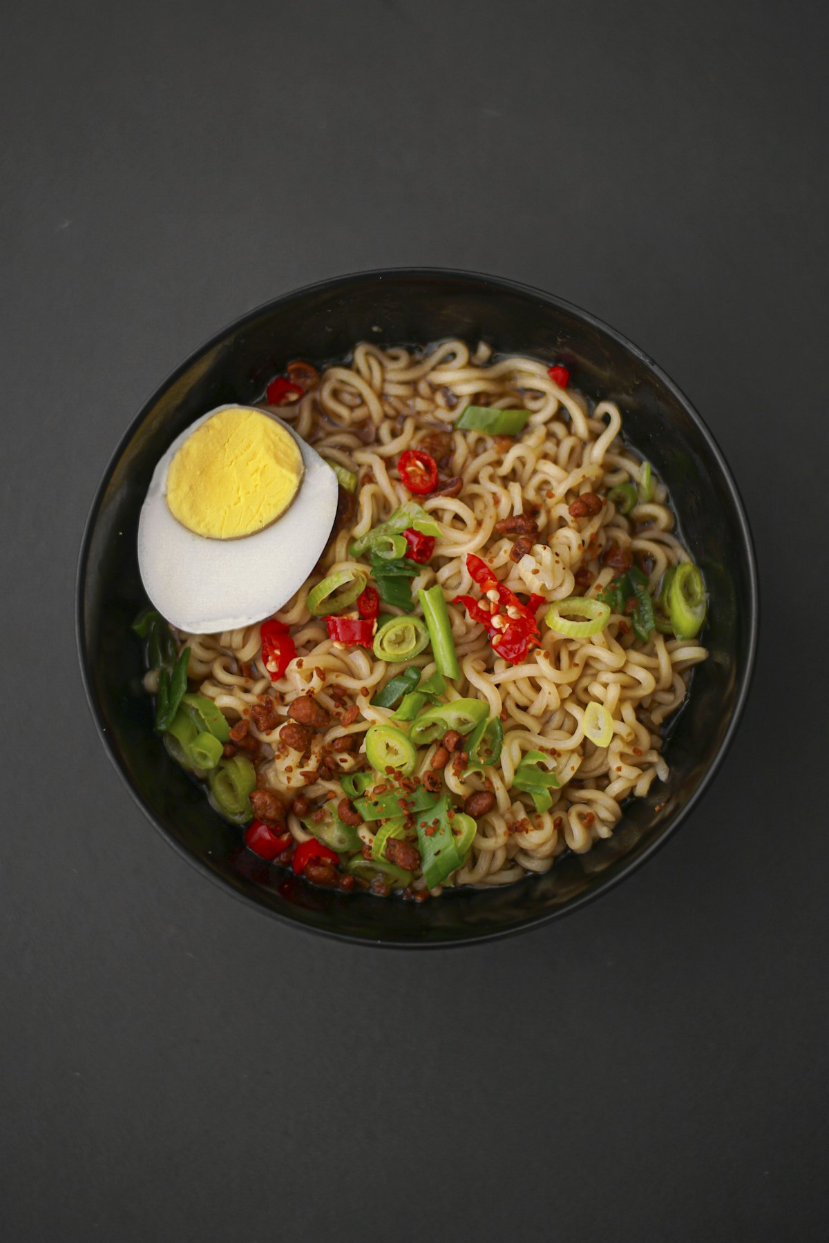 Dampfende Schüssel Ramen in einer schwarzen Schale, von oben fotografiert, mit Ei, Chili und Frühlingszwiebeln