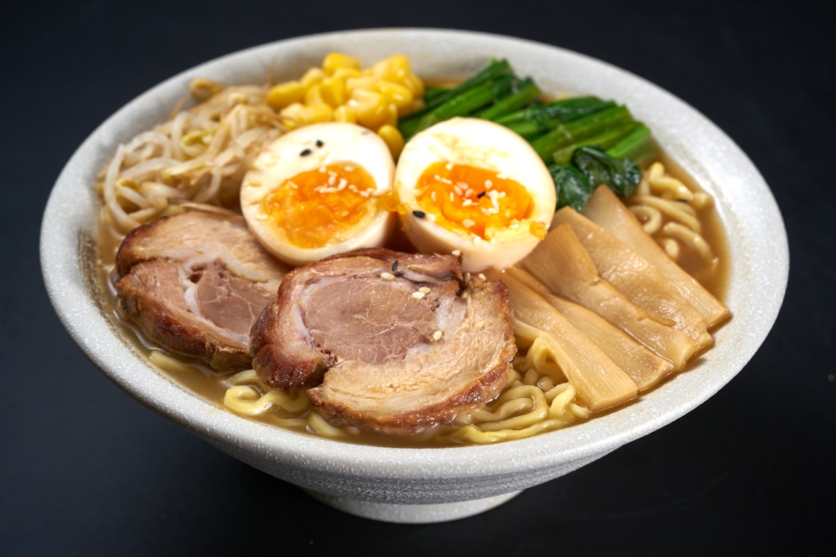 Schüssel Tonkotsu-Ramen mit zwei Scheiben Chashu, halbiertem Ei, Menma und Spinat auf dunklem Grund