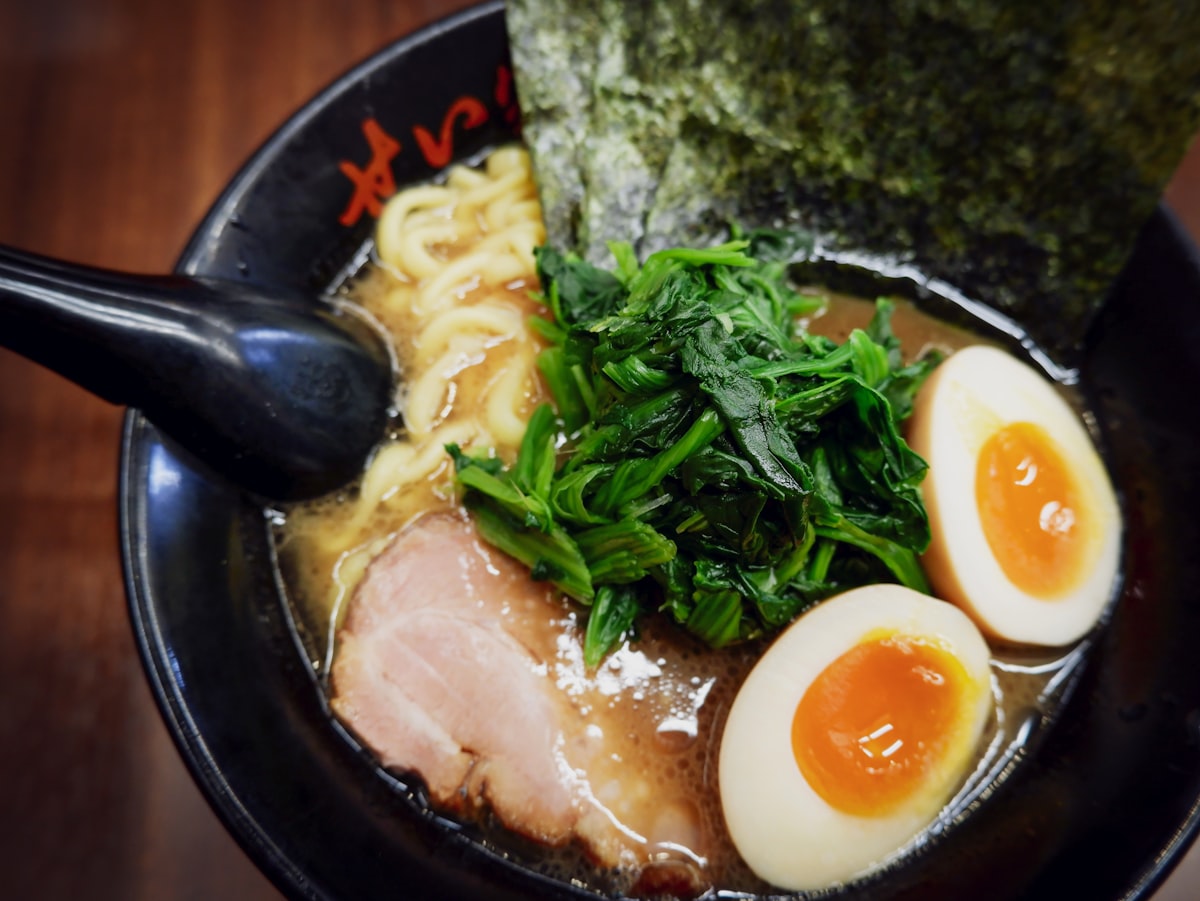 Nahaufnahme einer Schüssel Shoyu-Ramen in dunkler Schale mit Nori, Spinat, Chashu und weichem Ei